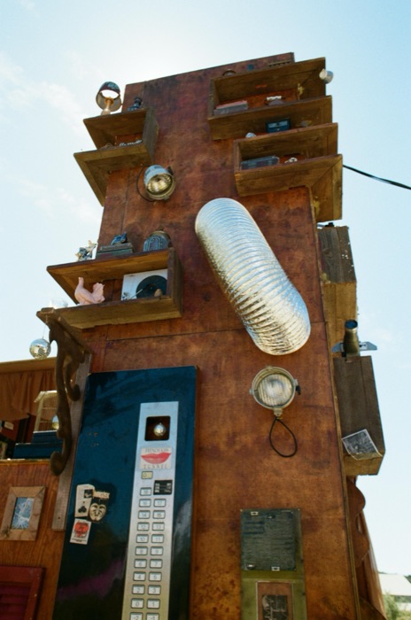 Rusted tower facade with found-object shelving and a salvaged elevator panel