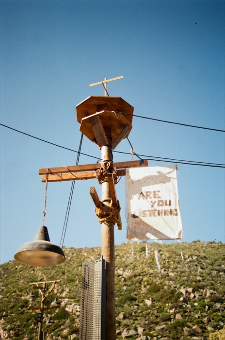 Hand-carved Are You Listening signage post against open sky