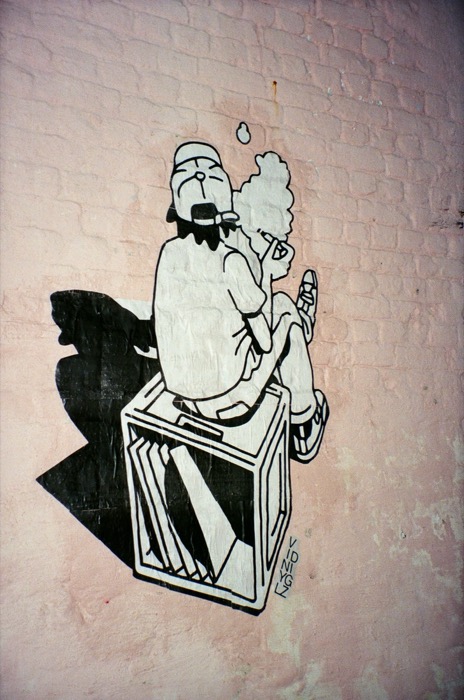 Solo wheatpaste figure smoking atop a record crate, close-up detail